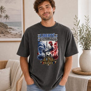 Puede incluir: Una camiseta de manga corta gris carb&oacute;n con un estampado gr&aacute;fico en el pecho que incluye el texto LIBERT&Eacute; &Eacute;GALIT&Eacute;, un gallo, la Torre Eiffel, un bal&oacute;n de f&uacute;tbol y un escudo con la palabra FRANCE en colores azul, blanco y rojo.