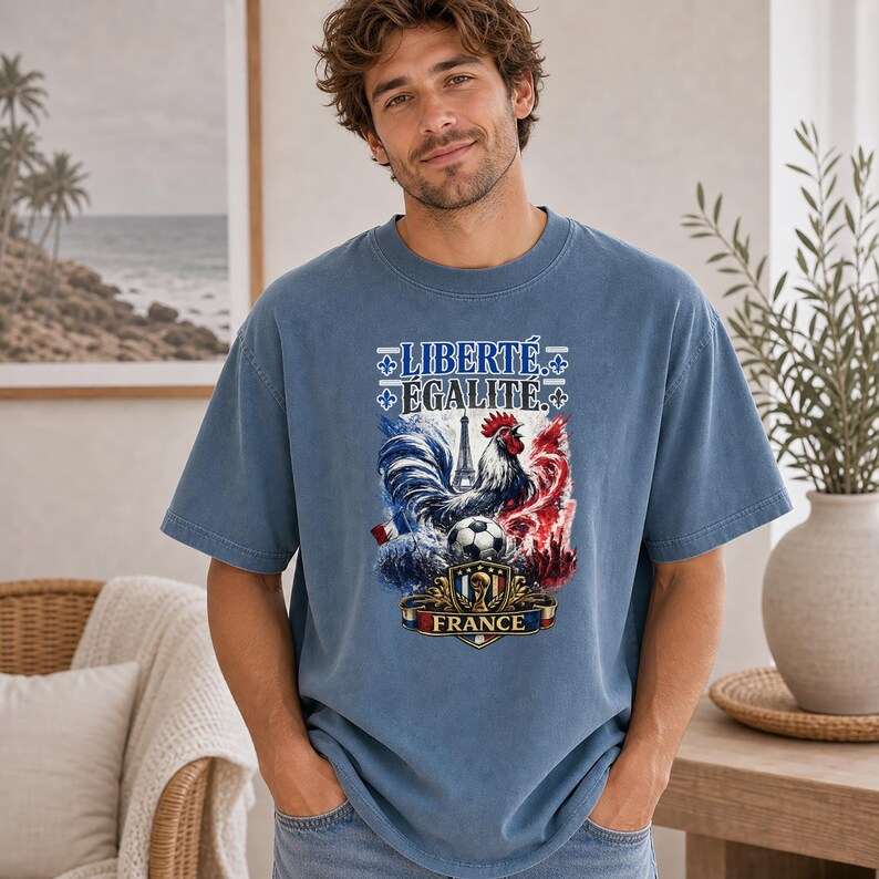 Puede incluir: Una camiseta azul de manga corta con un estampado gr&aacute;fico que incluye el texto LIBERT&Eacute; &Eacute;GALIT&Eacute; y FRANCE. El dise&ntilde;o presenta un gallo, un bal&oacute;n de f&uacute;tbol, la Torre Eiffel y s&iacute;mbolos de flor de lis en tonos rojo, blanco y azul.