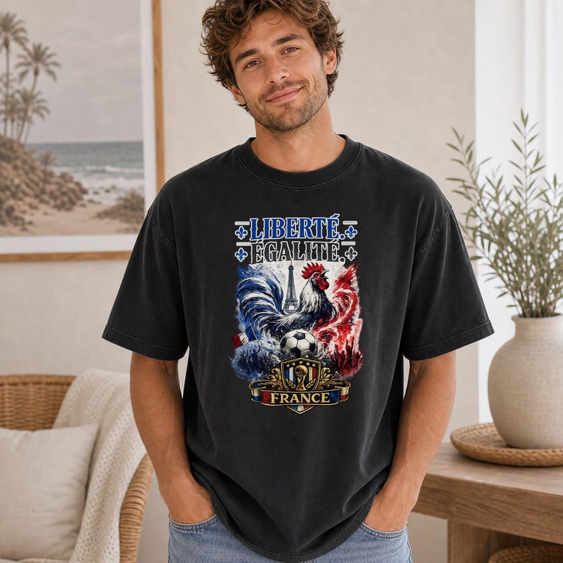 Puede incluir: Una camiseta negra de manga corta con un estampado gr&aacute;fico de un gallo, un bal&oacute;n de f&uacute;tbol, la Torre Eiffel y el texto "LIBERT&Eacute; &Eacute;GALIT&Eacute;" sobre un emblema de escudo con la palabra "FRANCE" en la parte inferior, en colores azul, blanco y rojo.
