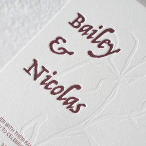 May include: A white card with deep red letterpress text reading Bailey & Nicolas. The card features a subtle, colourless embossed floral design in the background and partial text at the bottom reading HER WITH THEIR FAN U TO CELEBRA.