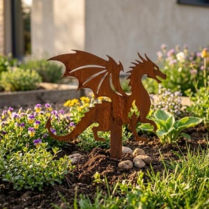 May include: A rusty brown metal dragon garden stake with outstretched wings and a long tail. The dragon is standing in a garden bed with green grass, colorful flowers, and small rocks. The dragon is a decorative garden ornament.