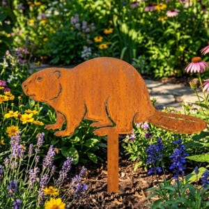 May include: A rusty brown metal beaver garden stake. The beaver is depicted in profile, with a detailed tail and paws. The stake is placed in a garden with colorful flowers.