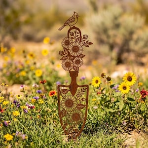 May include: A rust-colored metal garden stake shaped like a hand trowel, featuring intricate laser-cut designs of sunflowers and leaves on the blade and handle, topped with a small bird silhouette perched at the very peak of the metal structure.
