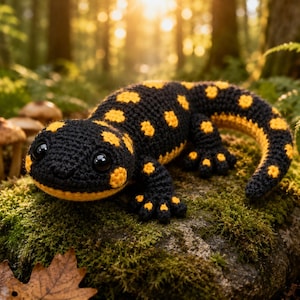 May include: A crocheted salamander toy featuring a black body with bright yellow spots, a rounded head with large black plastic eyes, and a curved tail. The textured yarn surface shows detailed stitching throughout the entire creature.