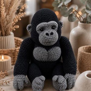 May include: A handcrafted crochet gorilla toy featuring a dark black body with contrasting light gray yarn detailing on the face, chest, hands, and feet. The stuffed animal has round black eyes and a textured, stitched appearance throughout its form.