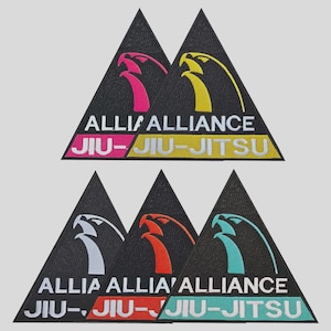 May include: A collection of triangular patches with the text "ALLIANCE JIU-JITSU". Each patch features a stylized eagle design in various colors, including pink, yellow, white, orange, and teal, set against a black background.