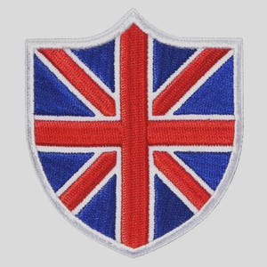 May include: Embroidered patch in the shape of a shield, featuring the Union Jack flag design. The patch has a white border, with a blue background and red cross and diagonal stripes. This patch is suitable for jackets, bags, or other fabric items.