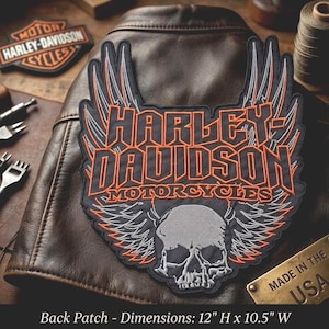 May include: A large embroidered Harley-Davidson back patch featuring a central skull graphic, orange and grey winged accents, and bold lettering. The patch measures 12 inches high by 10.5 inches wide and is displayed on a brown leather jacket.