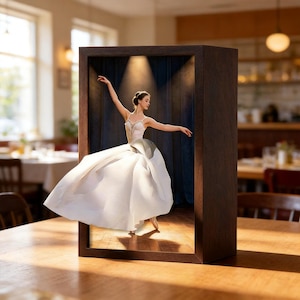 May include: A wooden display box with a ballerina figurine. The ballerina wears a white dress and is captured mid-dance. The backdrop is a dark blue curtain, and the scene is lit by spotlights. The box is on a wooden table.