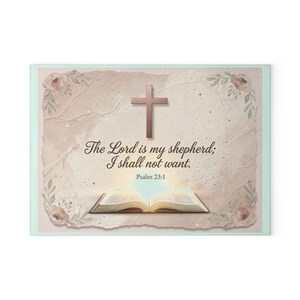 Könnte beinhalten: Rechteckiger dekorativer Druck mit einem Kreuz, floralen Akzenten und dem Text "Der Herr ist mein Hirte; mir wird nichts mangeln. Psalm 23,1." Das Design beinhaltet ein offenes Buch mit hellem Licht.