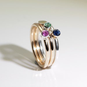 Może przedstawiać: Zestaw pierścionk&oacute;w do układania w stosy w odcieniach złota i srebra, każdy z kamieniem szlachetnym. Kamienie szlachetne są w kolorze granatowym, żywej zieleni i jasnor&oacute;żowym. Pierścionki są prezentowane na białej powierzchni.