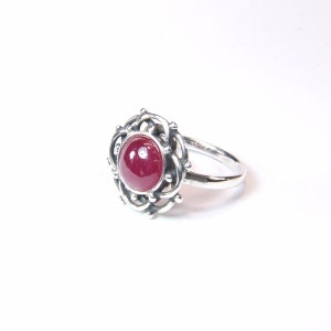 May include: A silver ring featuring a red gemstone set within a delicate, intricate design.