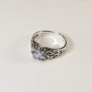 May include: A silver ring with a filigree design and a light purple gemstone. The ring is marked "sterling" on the inside.