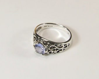 May include: A silver ring with a filigree design and a light purple gemstone. The ring is marked "sterling" on the inside.