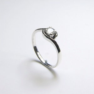 May include: A silver ring with a single, clear gemstone set in a twisted band.