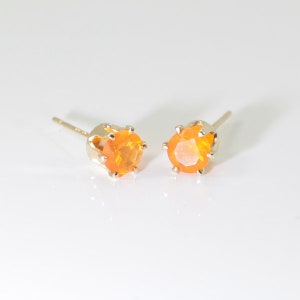 May include: A pair of gold stud earrings with orange opal gemstones. The earrings have a simple, classic design.