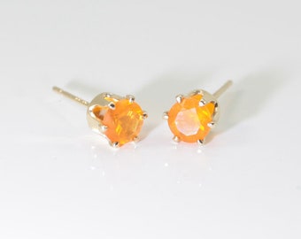 May include: A pair of gold stud earrings with orange opal gemstones. The earrings have a simple, classic design.