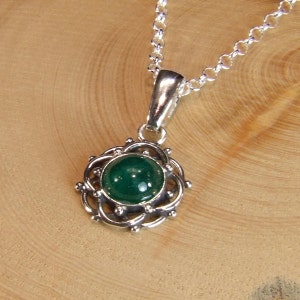 K&ouml;nnte beinhalten: Eine silberne Halskette mit einem gr&uuml;nen Edelstein-Anh&auml;nger. Der Anh&auml;nger ist ein runder Cabochon-Stein, der in einem filigranen Silberdesign gefasst ist.