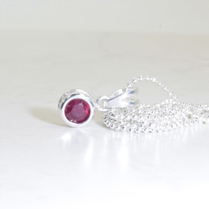 May include: A silver chain necklace with a small round pendant featuring a red gemstone.