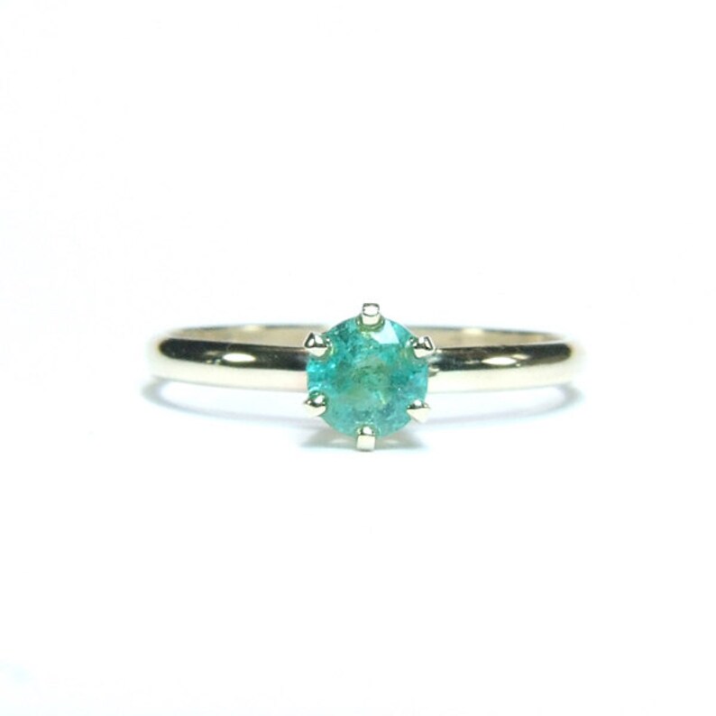 Pode incluir: Um anel de ouro com uma pedra preciosa redonda, verde-azulado claro. A pedra preciosa &eacute; engastada com seis garras. A banda do anel &eacute; de ouro polido simples. O anel est&aacute; centrado num fundo branco.