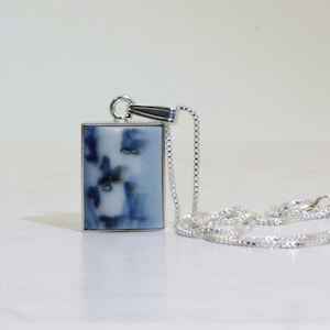 May include: A silver chain necklace with a rectangular pendant featuring a blue and white ceramic design.