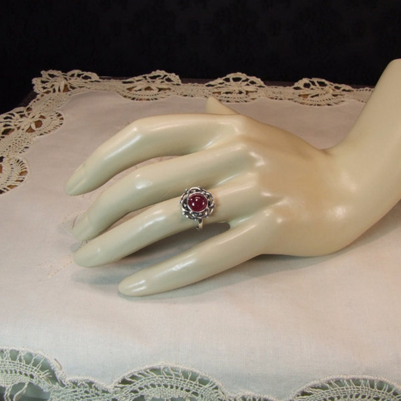 Puede incluir: Un anillo de plata con una piedra preciosa roja engastada en un dise&ntilde;o tejido.