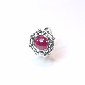 Puede incluir: Un anillo de plata con una piedra preciosa de rub&iacute; rojo engastada en un dise&ntilde;o delicado e intrincado.