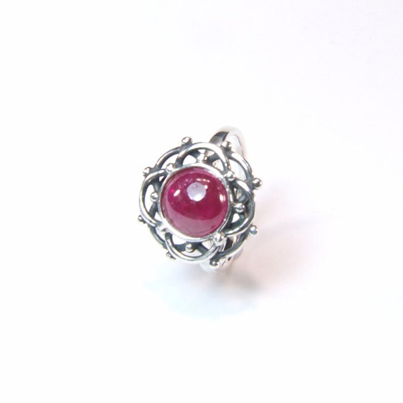 Puede incluir: Un anillo de plata con una piedra preciosa de rub&iacute; rojo engastada en un dise&ntilde;o delicado e intrincado.