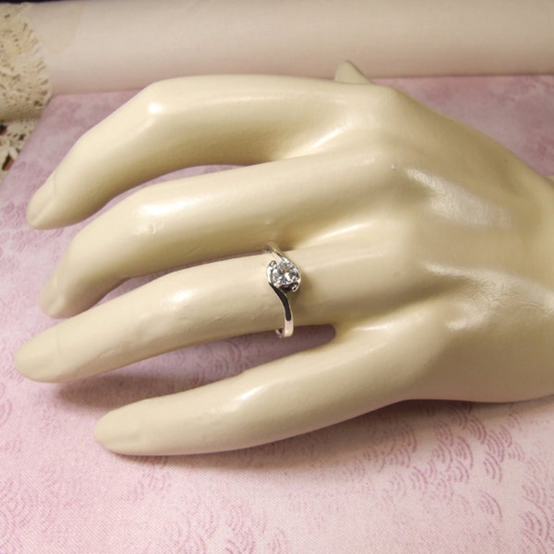 May include: A silver ring with a single, clear, round gemstone set in a curved band.