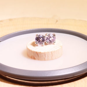 May include: A pair of silver stud earrings with round, light purple gemstones.