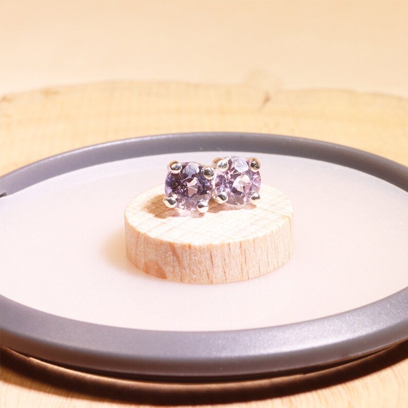 May include: A pair of silver stud earrings with round, light purple gemstones.