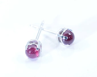 May include: A pair of silver stud earrings with small, round, red gemstones.