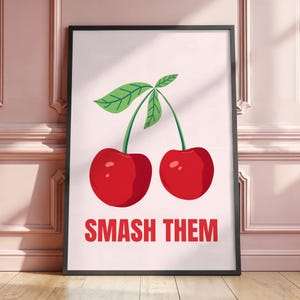 Peut inclure: Impression d'art encadrée représentant deux cerises rouges vives avec des tiges et des feuilles vertes sur fond rose clair. Le texte "SMASH THEM" est imprimé en rouge en bas de l'image.