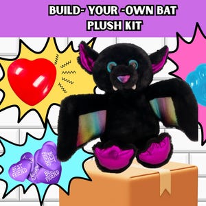May include: A 16 inch Build-Your-Own Bat Plush Kit featuring a black plush bat with rainbow-colored wing accents, pink inner ears, and bright pink feet. The kit includes a red heart, purple heart-shaped tokens, and a blue paw-shaped accessory.
