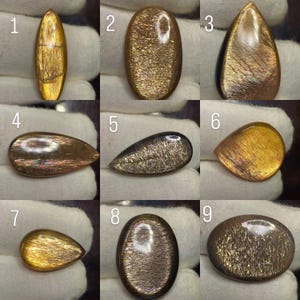 Può includere: Una collezione di nove cabochon di pietra del sole lucidati numerati da uno a nove, ognuno dei quali mostra un'avventurescenza dorata, bronzea e metallica unica. Le pietre variano nella forma, includendo tagli ovali, a goccia e a marquise.
