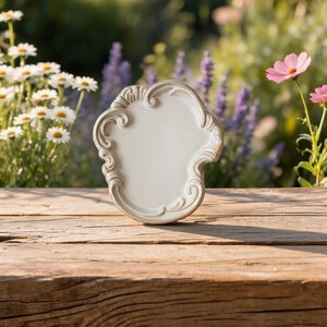 White ceramic trinket dish with scalloped baroque rim on cozy knit blanket