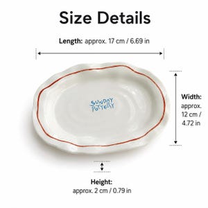 Top view of a white jewelry tray with red rim and blue Sunday Pottery text.