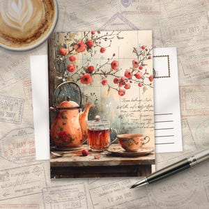 May include: A postcard with a watercolour illustration of a teapot, teacup, and glass of tea. The card features red flowers and script. A cup of coffee and a pen are also visible, suggesting a tea-themed setting.