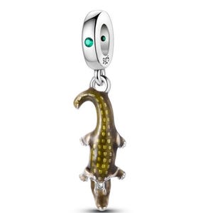 Pode incluir: Um berloque de prata com um pingente de crocodilo pendurado com detalhes em esmalte verde e marrom. A peça possui um topo circular com uma pequena pedra verde incrustada e a gravação S925, projetada para pulseiras ou colares.