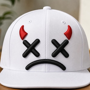 Pode incluir: Um boné de beisebol branco com um gráfico bordado na frente. O design consiste em dois olhos pretos em forma de X, uma boca preta curva e dois pequenos chifres de diabo vermelhos posicionados acima dos olhos.