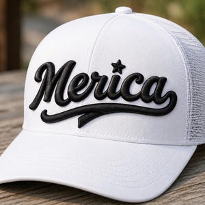 Może przedstawiać: Biała czapka typu trucker z siateczkowym tyłem i pełnym przednim panelem. Z przodu znajduje się napis Merica wykonany wypukłym, czarnym haftem w stylu pisma odręcznego, z małą czarną gwiazdką umieszczoną nad literą i, co nadaje całości wyrazistą fakturę.
