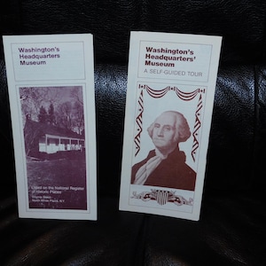 May include: Two brochures from Washington's Headquarters Museum. One features a sepia-toned image of a building, the other a portrait of George Washington. Text includes "A Self-Guided Tour" and museum name.