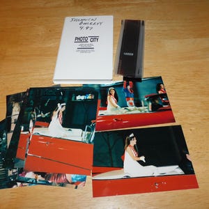 May include: A white envelope labeled "SHANNON DOHERTY 4.97 PHOTO CITY" with a strip of 35mm film and several color photographs showing a person in a white dress and tiara riding in a red convertible car during a parade or public event.