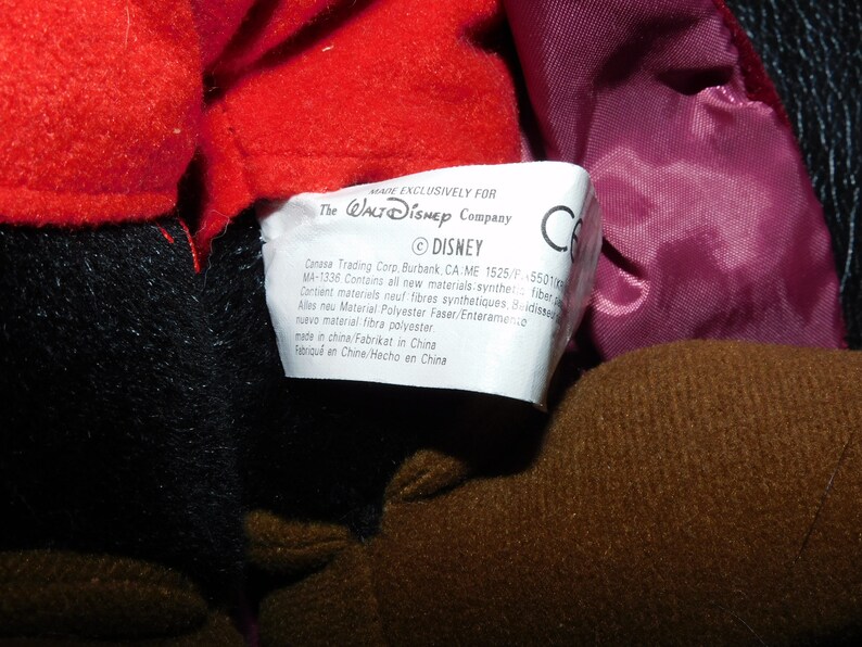 May include: Close-up of a plush toy with red, black, and brown fabric. A white tag with text from The Walt Disney Company is visible. The tag includes the Disney logo and manufacturing information.