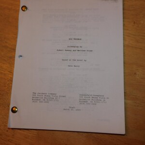 May include: A white screenplay titled Big Trouble, written by Robert Ramsey and Matthew Stone, based on the novel by Dave Barry. The document is dated March 23, 2009, and features two metal fasteners on the left side, with production company details.