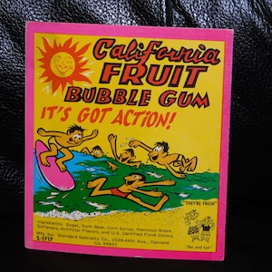 May include: A rectangular California Fruit Bubble Gum wrapper with a yellow background and pink border. The graphic features a sun, cartoon figures surfing and swimming in blue water, and the text: California Fruit Bubble Gum, It's Got Action!
