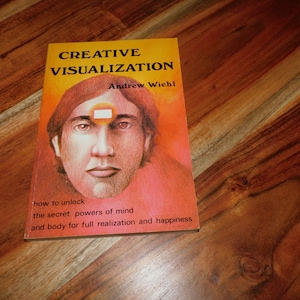 May include: A paperback book titled Creative Visualization by Andrew Wiehl. The cover features a warm orange and red gradient background with a central illustration of a human face and a small rectangular symbol on the forehead area.