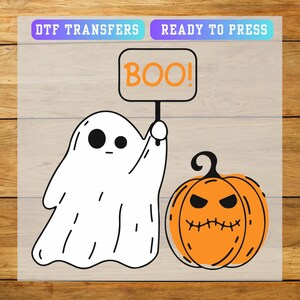 May include: A DTF transfer sheet featuring a white ghost holding a sign that says BOO! in orange letters, alongside an orange pumpkin with a black stem and a stitched mouth. The top of the sheet includes the text DTF TRANSFERS READY TO PRESS.