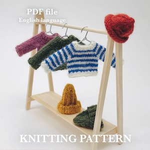 May include: A miniature wooden clothing rack displays several knitted items. There are sweaters in purple, green, and blue and white stripes, along with a red hat, a yellow hat, and a green hat. The text "PDF file English language" and "KNITTING PATTERN" are visible.