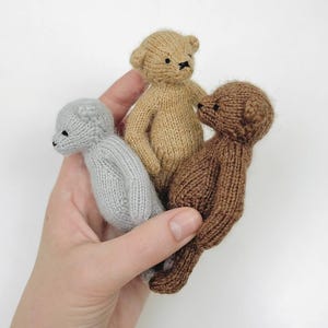 Peut inclure: Trois petits ours en peluche tricot&eacute;s en gris, beige et marron. Les ours ont des yeux et des nez cousus en noir. Les ours sont tenus dans une main sur fond blanc. Les ours mesurent environ 10 cm de haut.